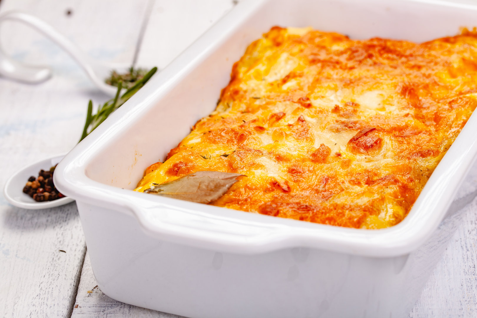 Potato gratin in white casserole dish on wooden rustic table. Close up Gratin de céleri rave