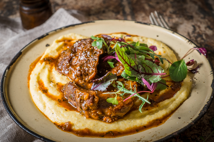 Delicious Braised Beef Served Over Creamy Polenta Garnished with Fresh Microgreens Escalope de veau, polenta et poêlé de champignons